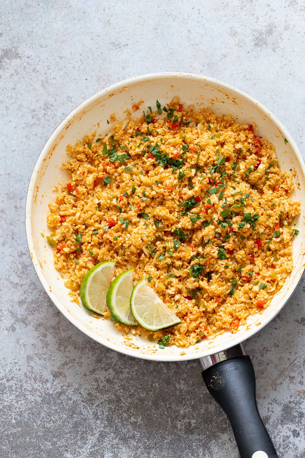 Spanish Cauliflower Rice overhead hot of a pan with Spanish cauliflower rice decorated with cilantro and lime slices