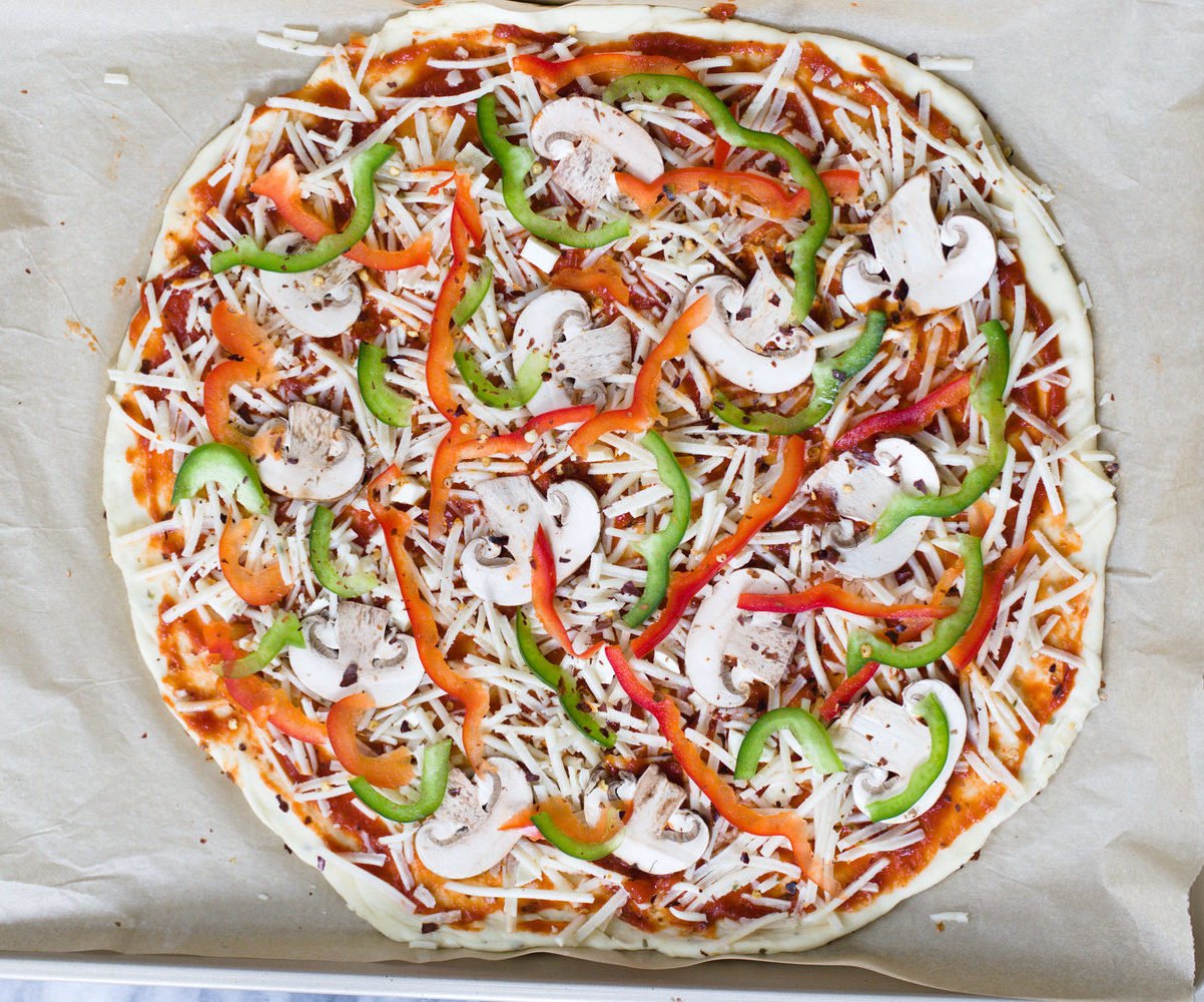 no yeast pizza dough  overhead shot of unbaked vegan pizza on a baking sheet topped with vegetables and vegan cheese shreds