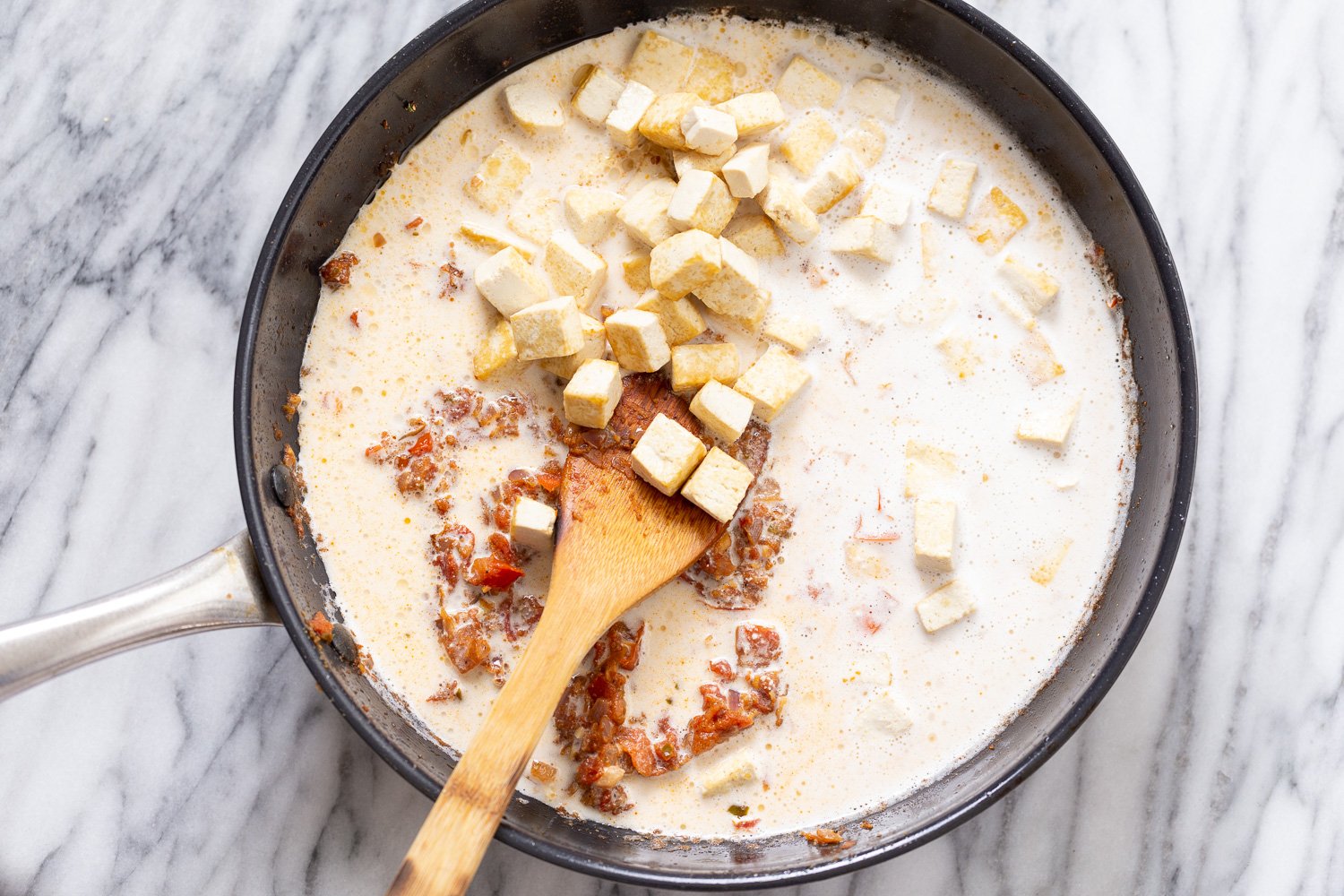 tofu in sauce tofu cubes and cashew cream being added to skillet to make creamy Indian tofu curry