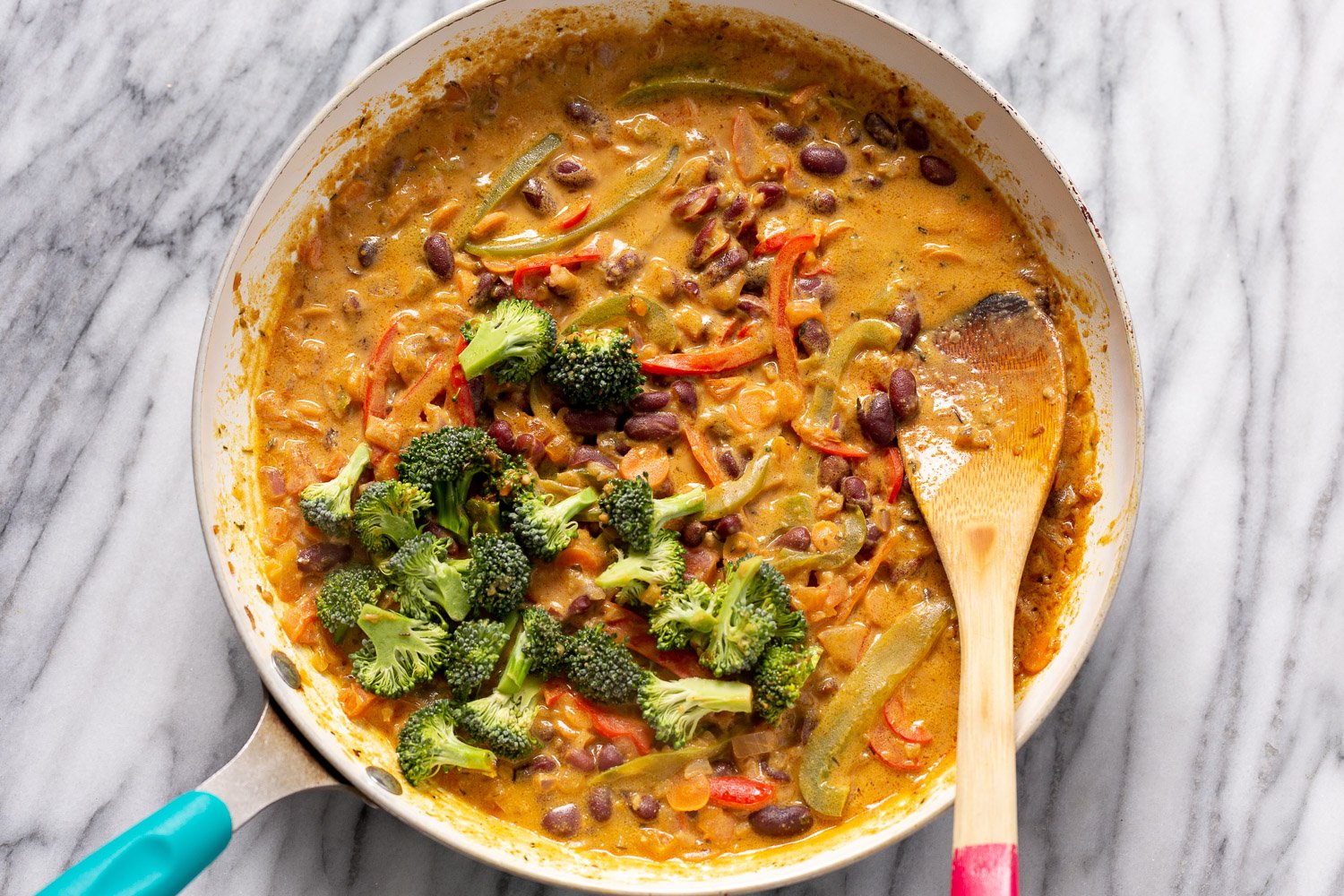 Peanut Stew broccoli florets being stirred into a pan with creamy vegan Peanut Stew