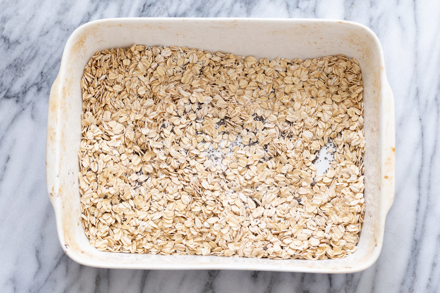 vegan baked oatmeal  overhead shot of a casserole dish filled with rolled oats and chia seeds