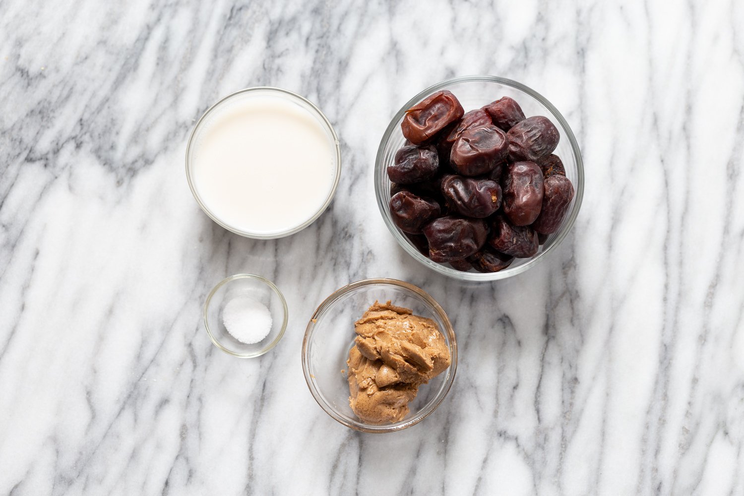 snickers recipe  small glass dishes with plant based milk, dates, nut butter and salt on a kitchen counter