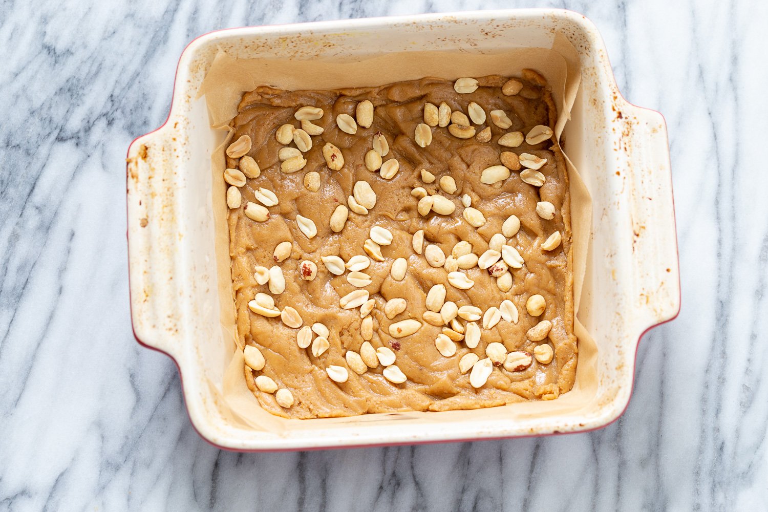 snickers bars recipe  peanuts being sprinkled on cookie base to make vegan snack bars