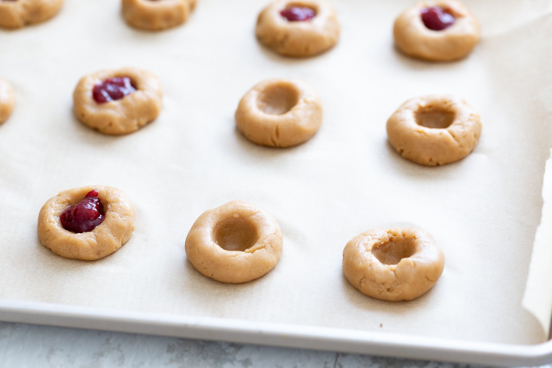thumbprint cookies cookie dough balls being indented and filled with jam to make thumbprint cookies
