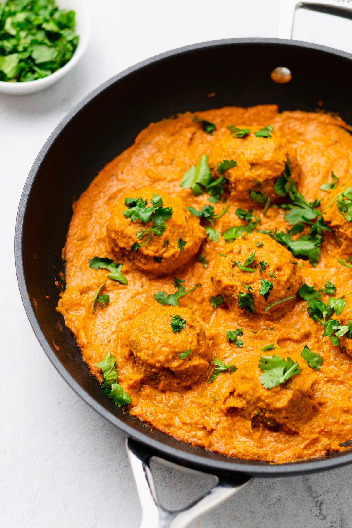 vegan malai kofta side view of a skillet with vegan malai kofta sprinkled with cilantro