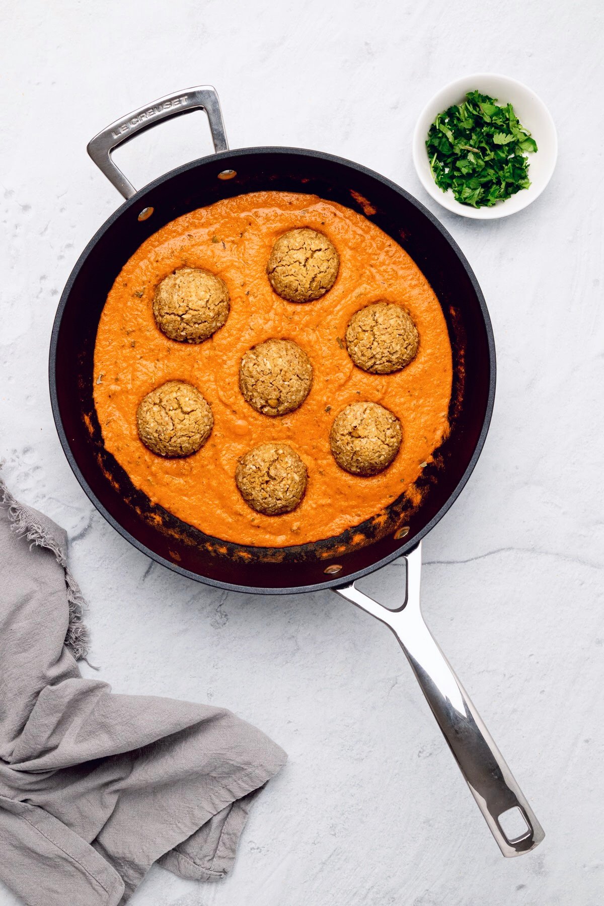 vegan malai kofta overhead shot of a skillet with vegan kofta in a dairy-free Indian gravy with chopped cilantro on the side