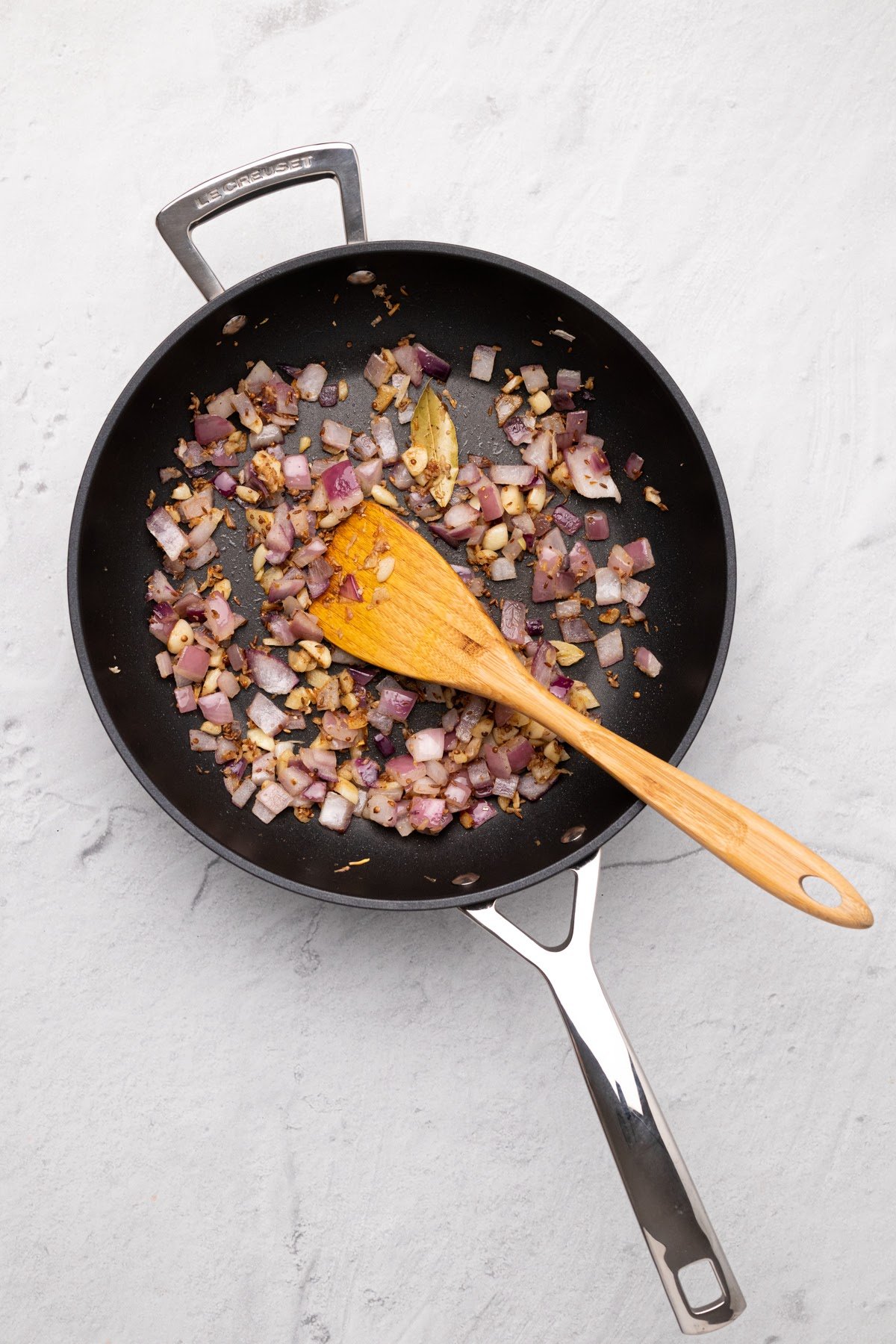 vegan malai kofta onions being stir-fried in a black skillet with spices to make malai kofta gravy