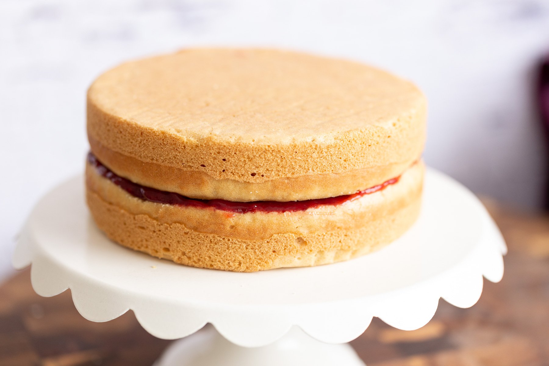 assembled vegan white cake filled with raspberry jam on a cake stand 