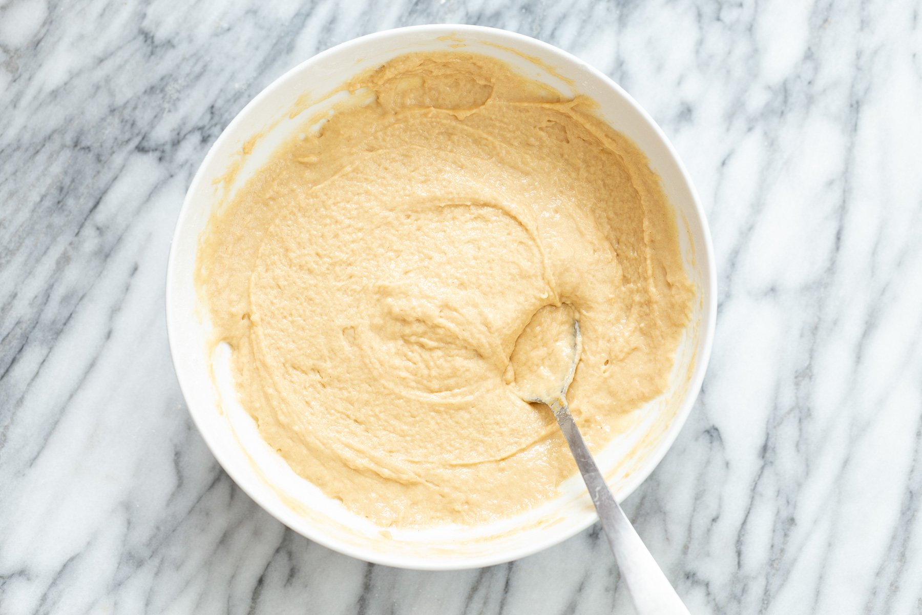 peanut butter and jelly cake  peanut butter cake batter being mixed with a metal spoon in a white mixing bowl