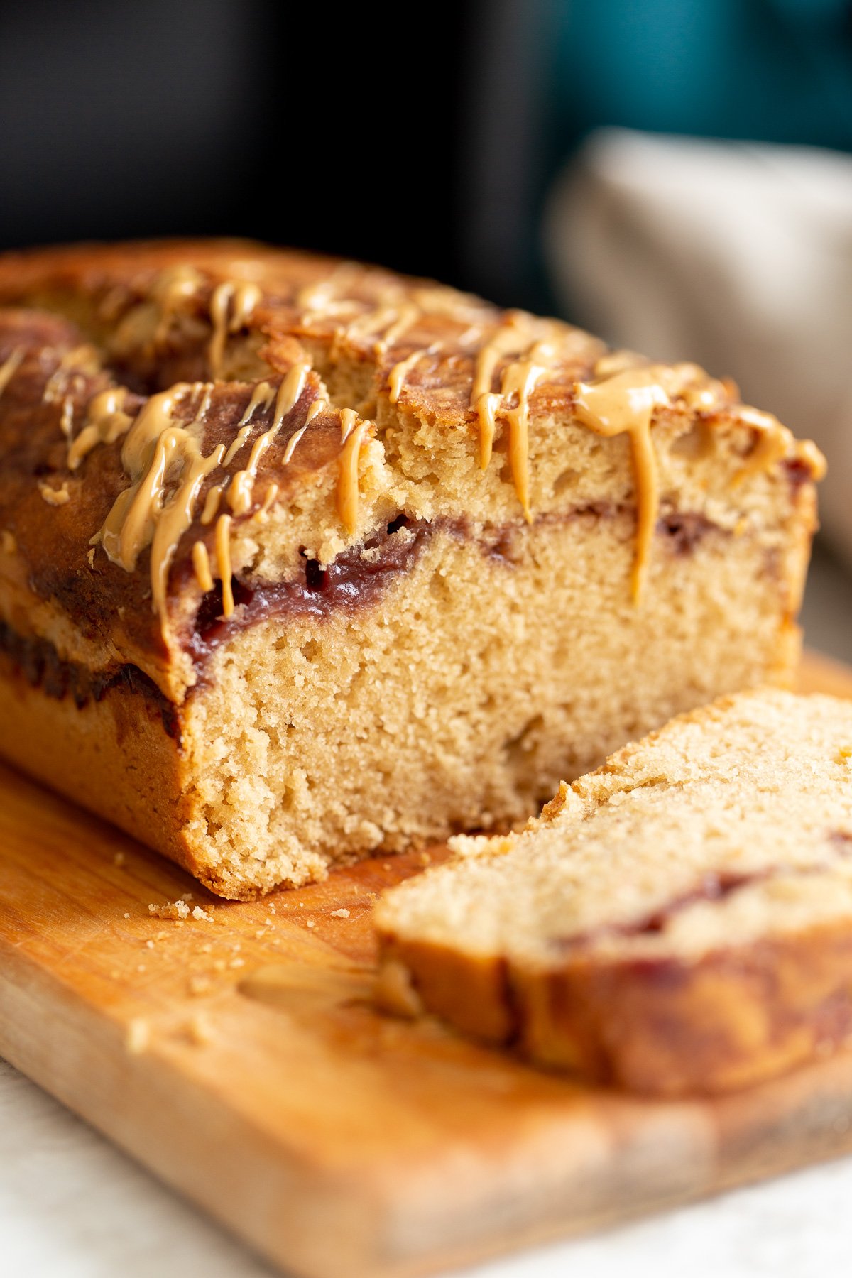 peanut butter and jelly cake  close up of a sliced vegan pb and j loaf cake drizzled with peanut butter on a cutting board