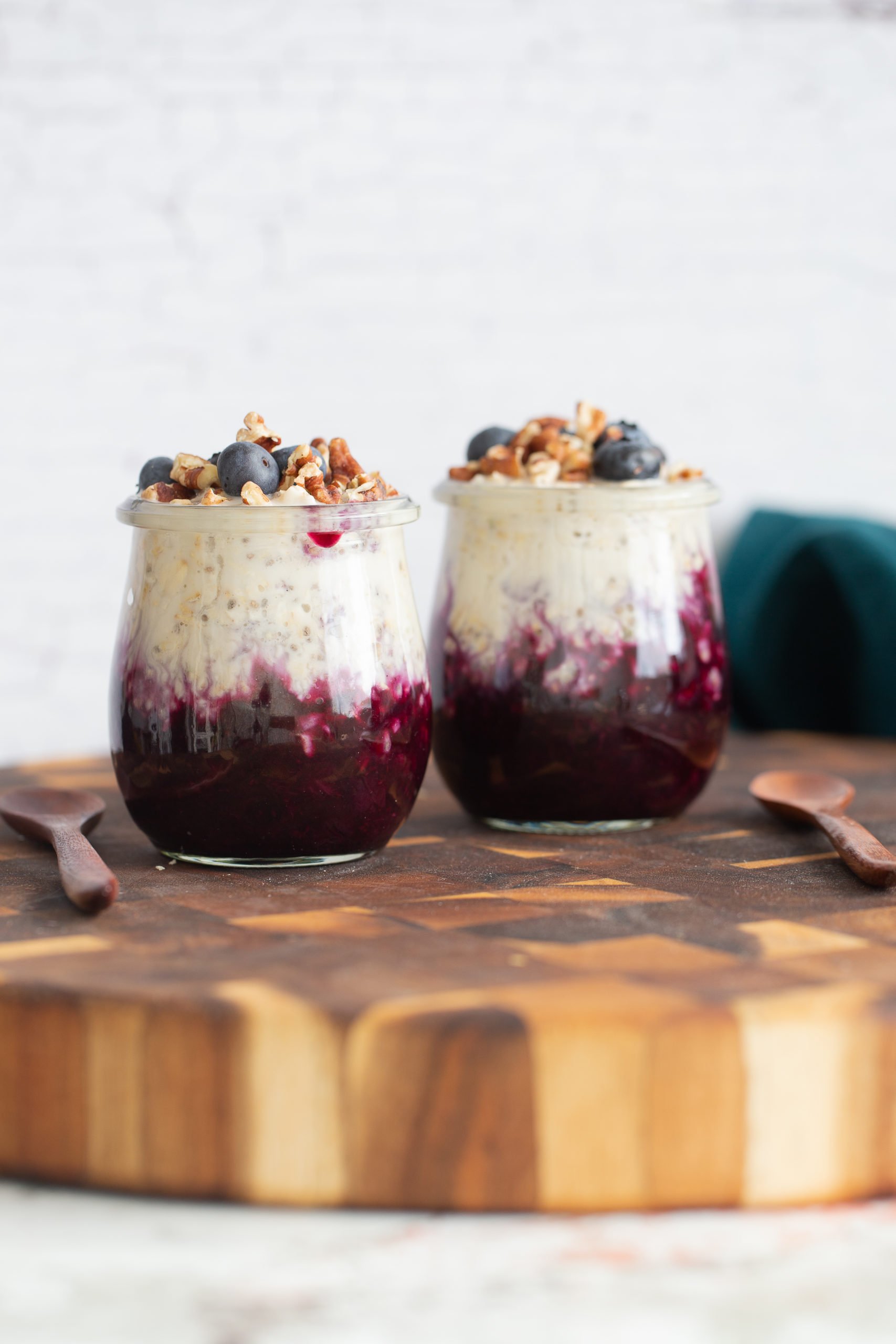blueberry overnight oats  side view of two jars of make ahead vegan blueberry muffin overnight oats on wooden board