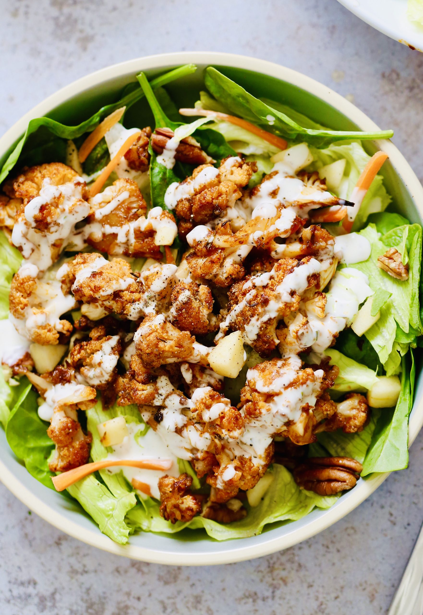 overhead shot of a salad bowl topped with bbq roasted cauliflower and vegan ranch dressing