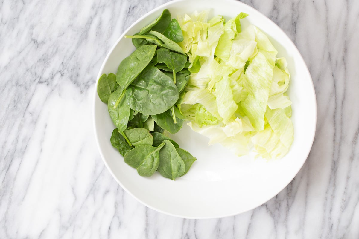 cauliflower salad  spinach and iceberg salad being arranged in a white bowl to make cauliflower salad bowl