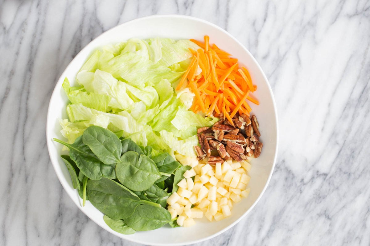 overhead shot of a salad bowl with spinach and iceberg lettuce, carrots, pecans and apples