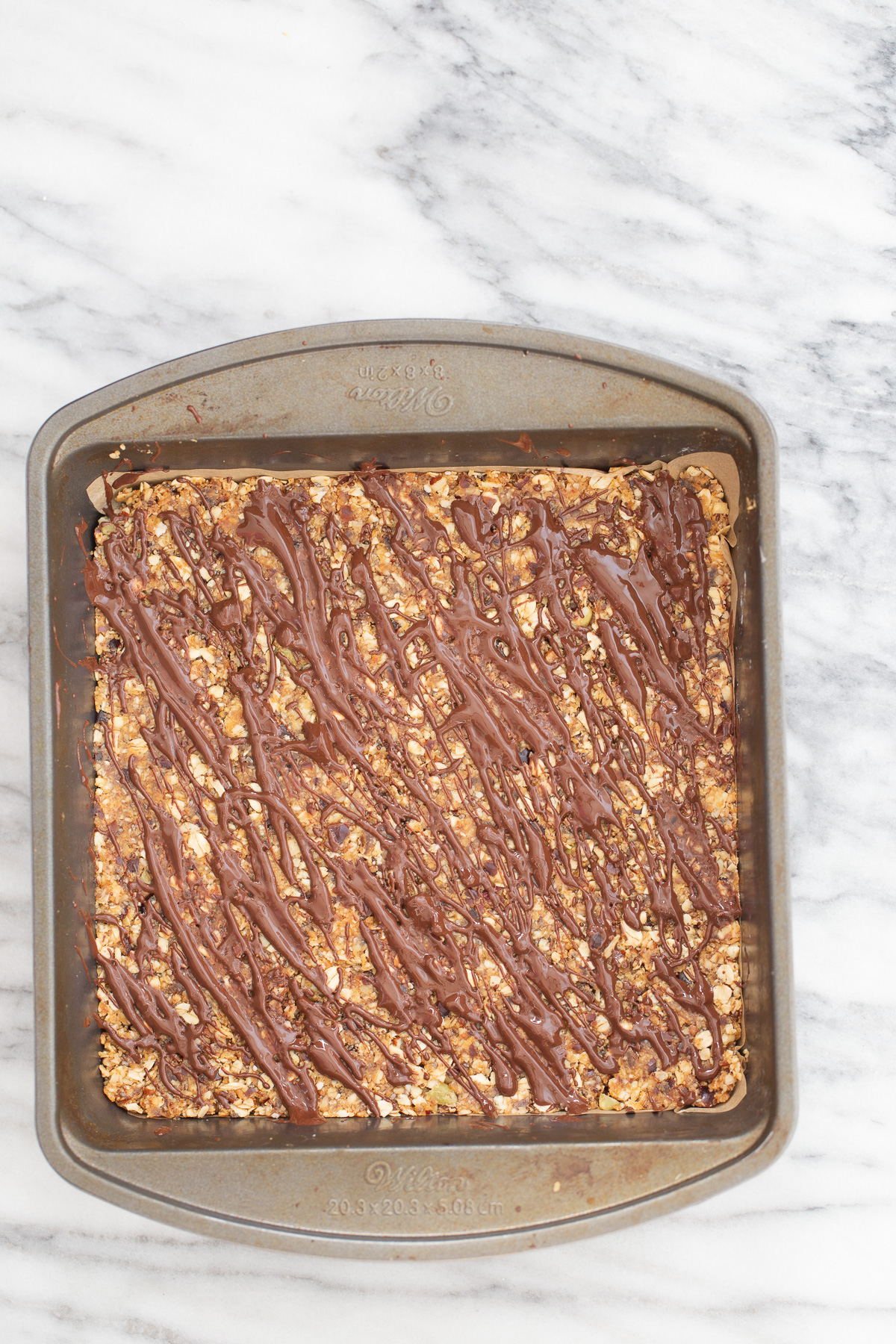 vegan date bars  overhead shot of a casserole dish with vegan coconut caramel date bars drizzled with melted chocolate