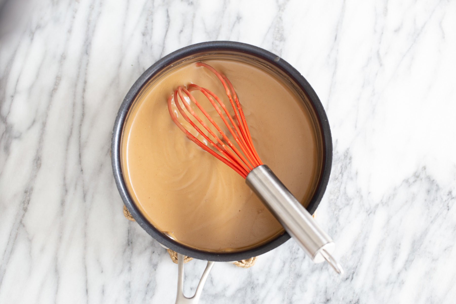peanut butter mousse base for making peanut butter mousse being whisked in a pot with a red whisk