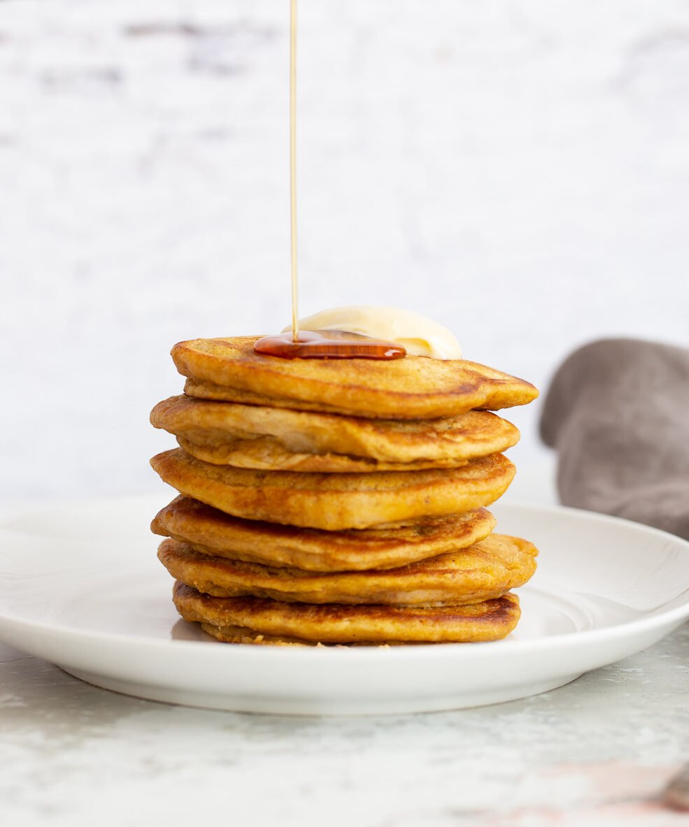 vegan pumpkin pancakes a stack of vegan pumpkin pancakes being drizzled with maple syrup