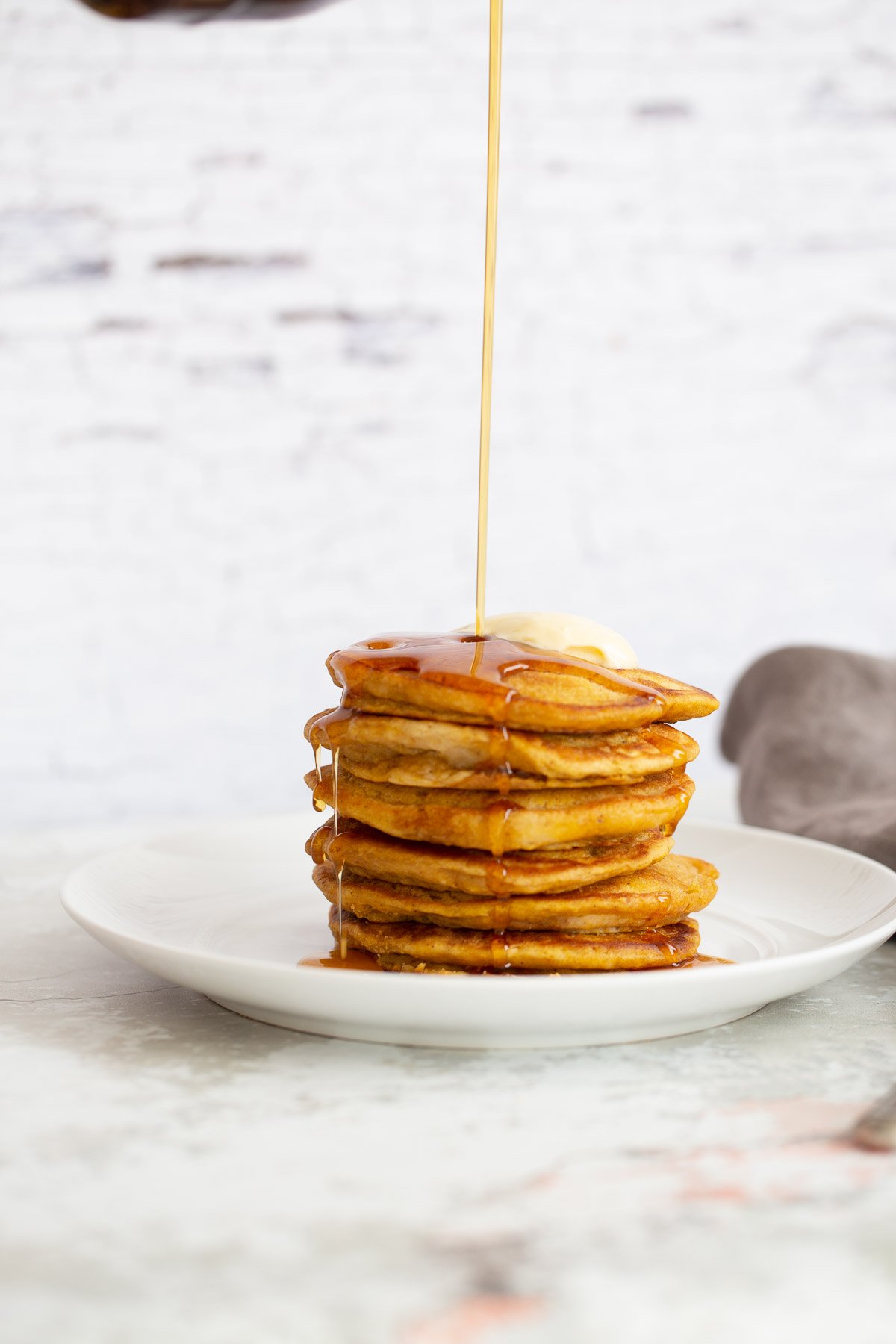 vegan pumpkin pancakes a stack of pancakes being drizzled with maple syrup