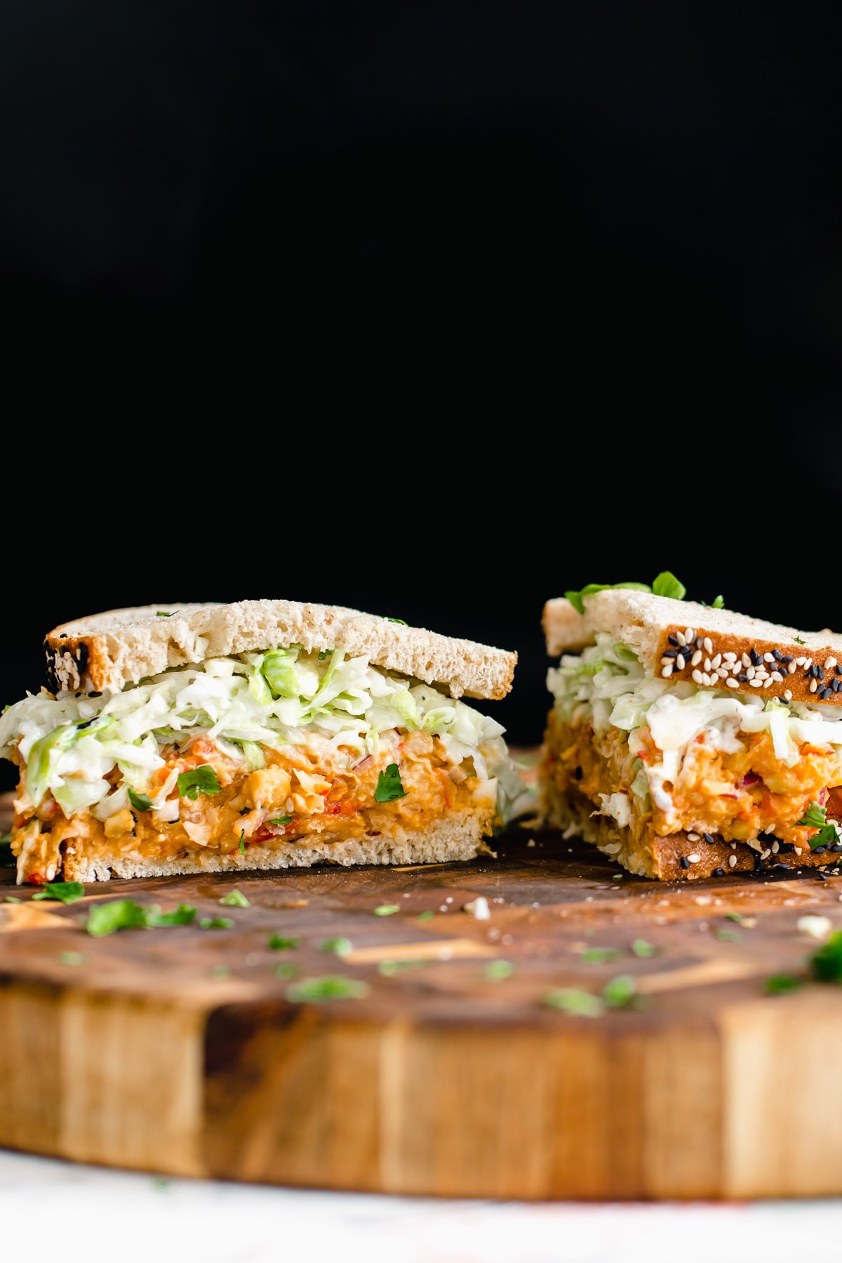 chickpea salad sandwich  a halved buffalo chickpea salad sandwich with slaw on a wooden chopping board