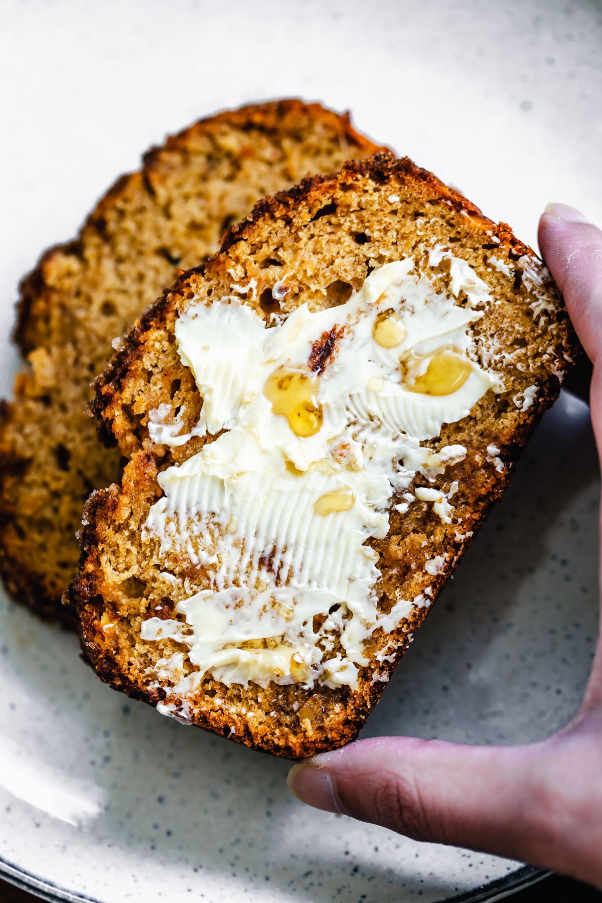 gingerbread banana bread a hand reaching for a buttered slice of vegan gingerbread banana bread
