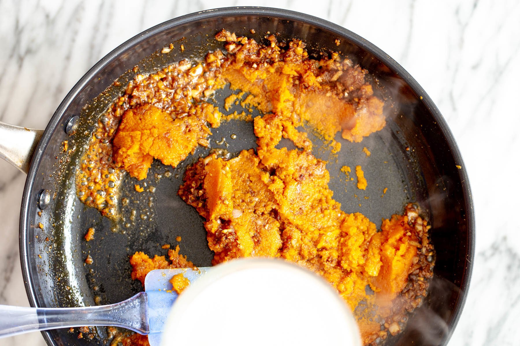 pumpkin curry  pumpkin puree being added to pan with tempered Indian spices