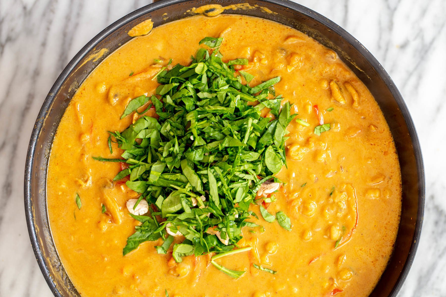 pumpkin curry  pumpkin chickpea curry being sprinkled with fresh herbs before serving
