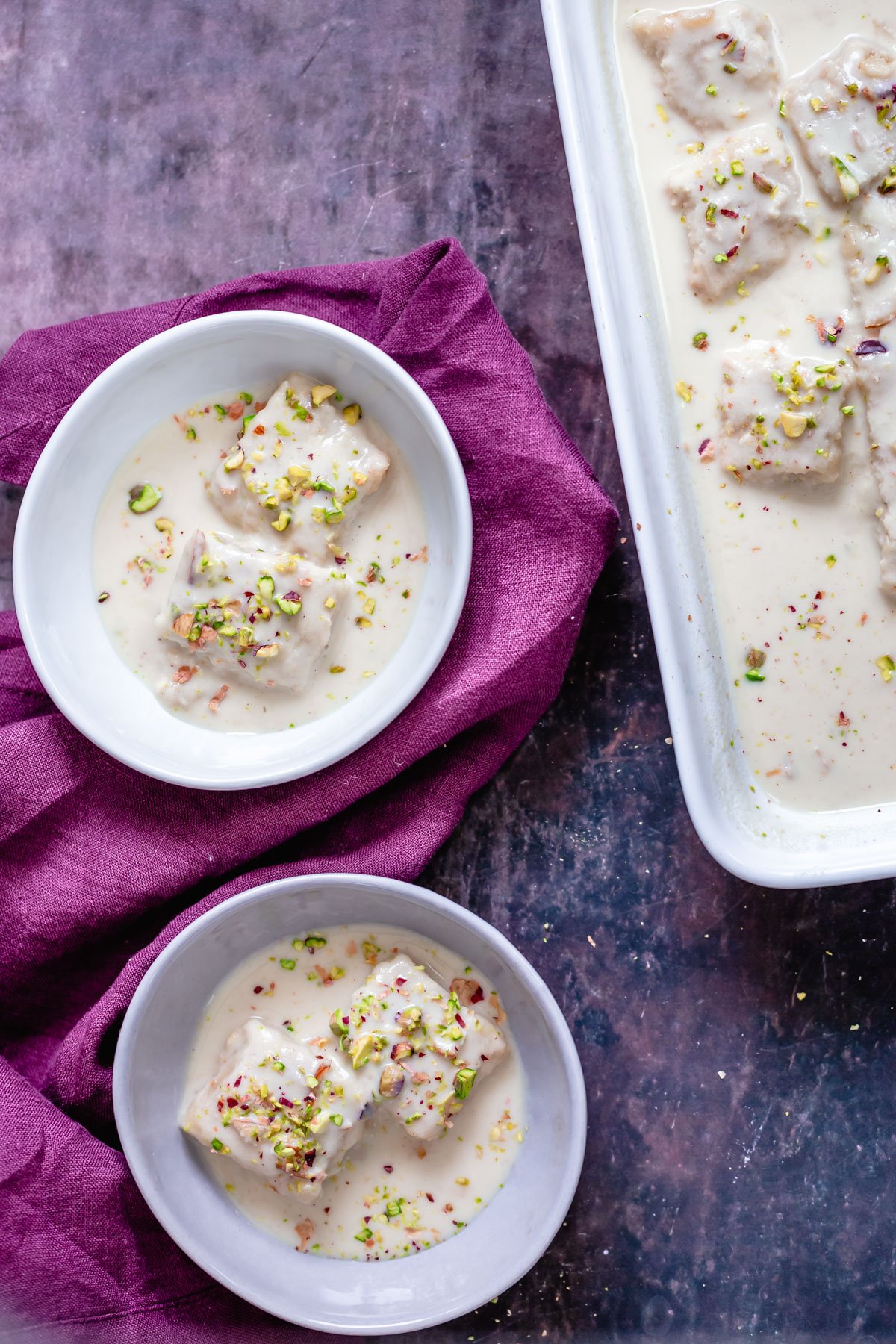 rasmalai cake two servings of two plates of vegan rasmalai cake in milk sauce sprinkled with pistachios
