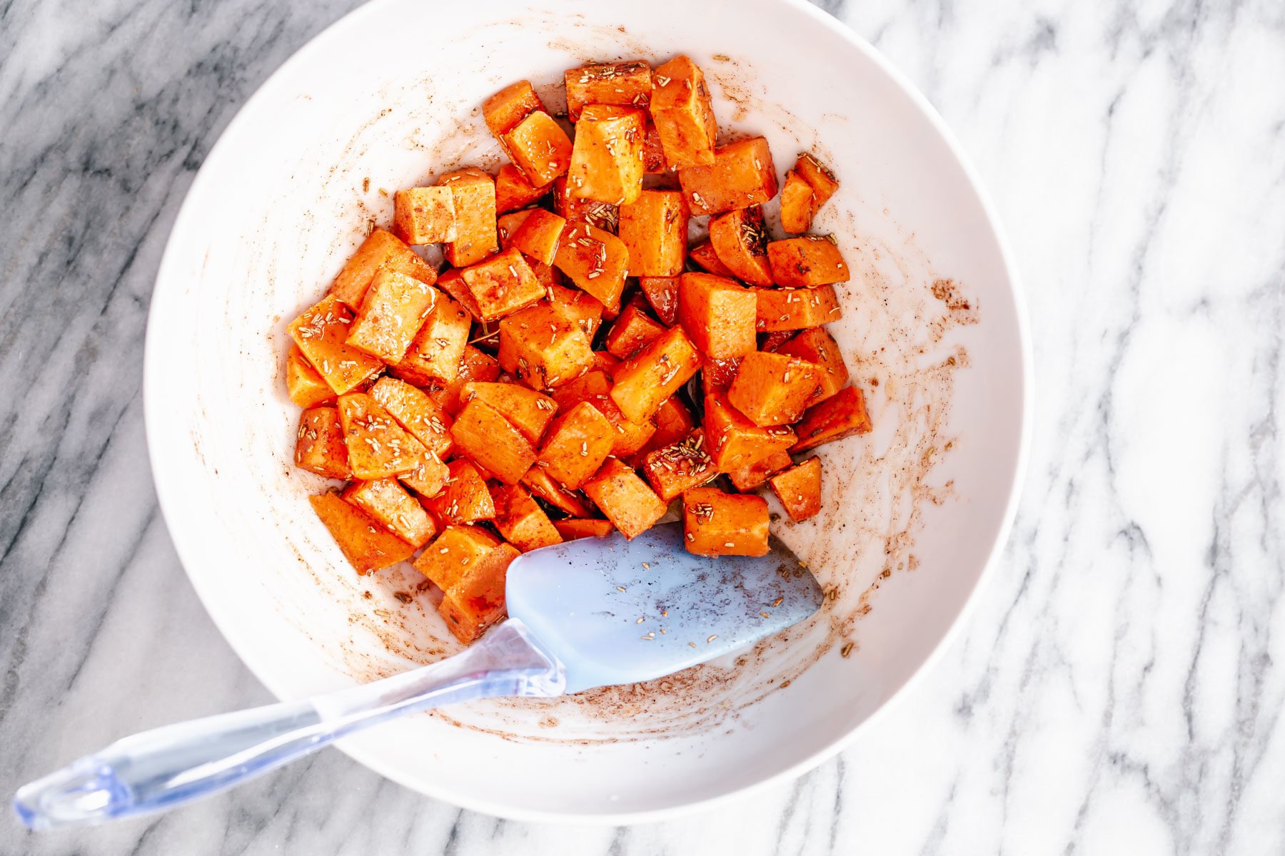 Thanksgiving sheet pan dinner sweet potato cubes being tossed in a white bowl
