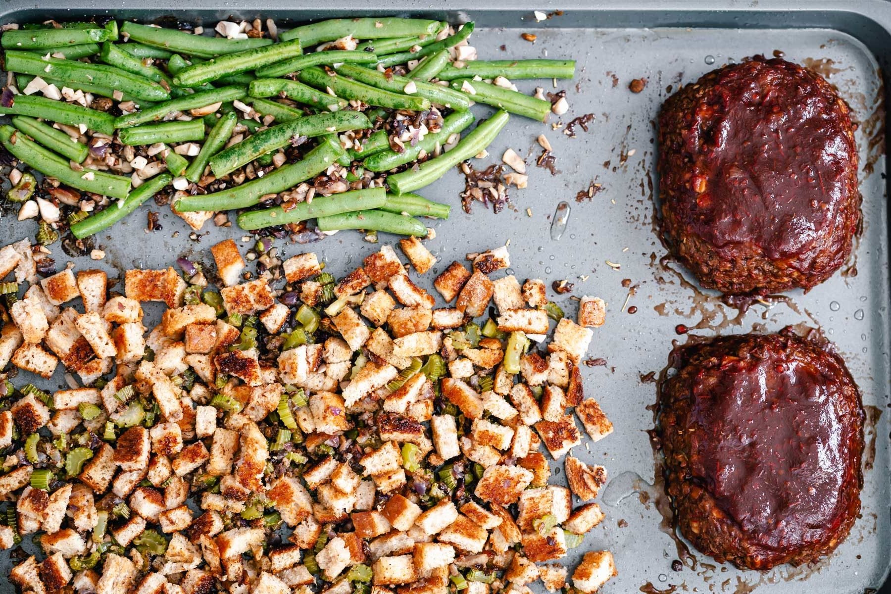 Thanksgiving sheet pan dinner baked vegan stuffing and green beans next to two small lentil meatloaves
