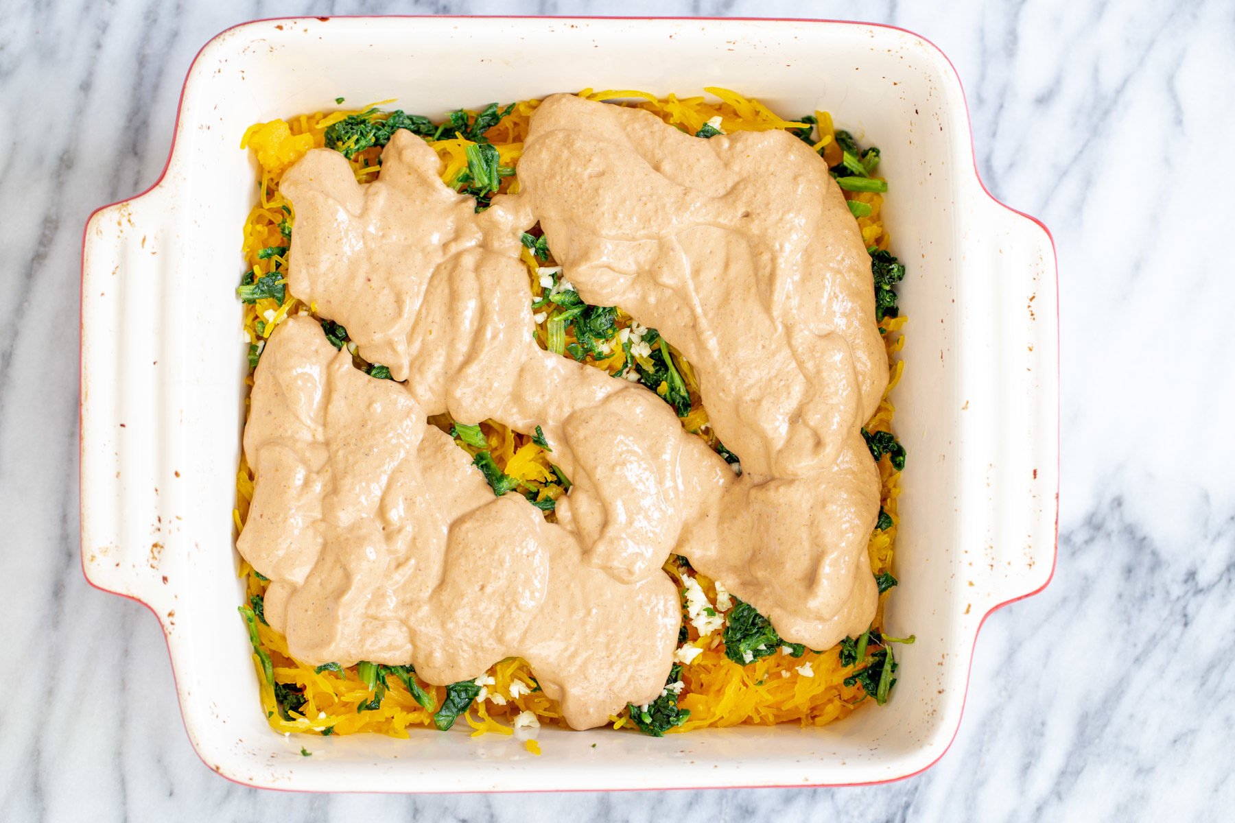 creamy vegan sun-dried tomato sauce being poured on top of spaghetti squash to make casserole