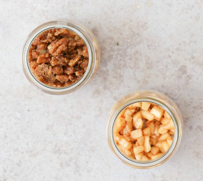 two small dessert glasses being layers to make apple pie overnight oats 