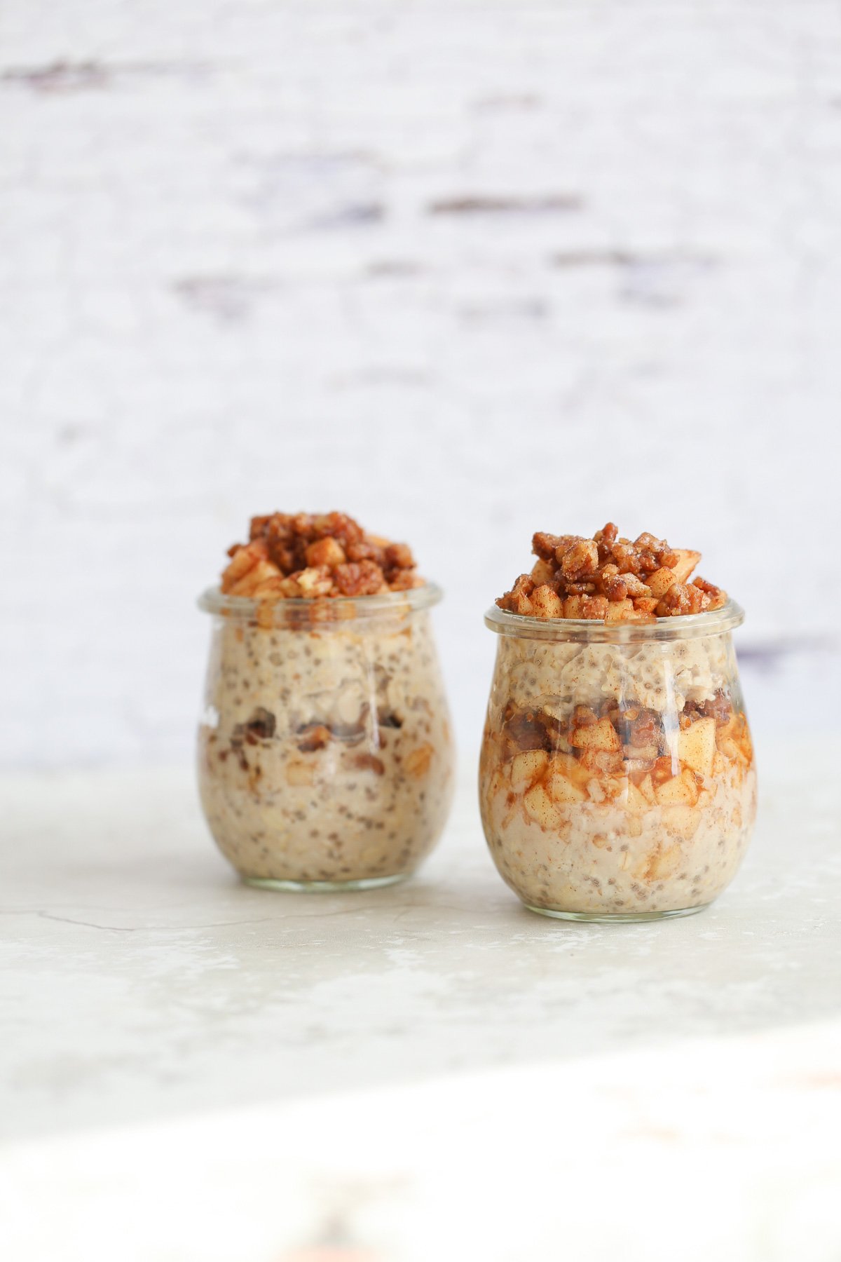 side view of two jars of apple pie overnight oats topped with stewed apples and candied pecans 