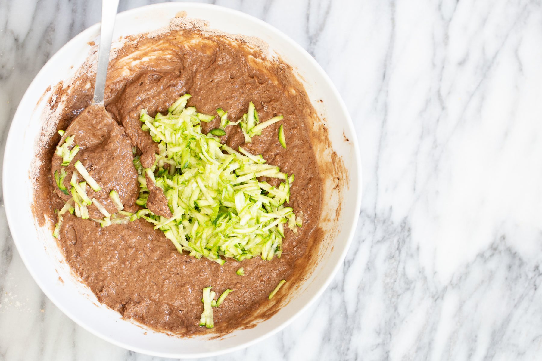chocolate zucchini bread shredded zucchini being added to chocolate cake batter in a white mixing bowl