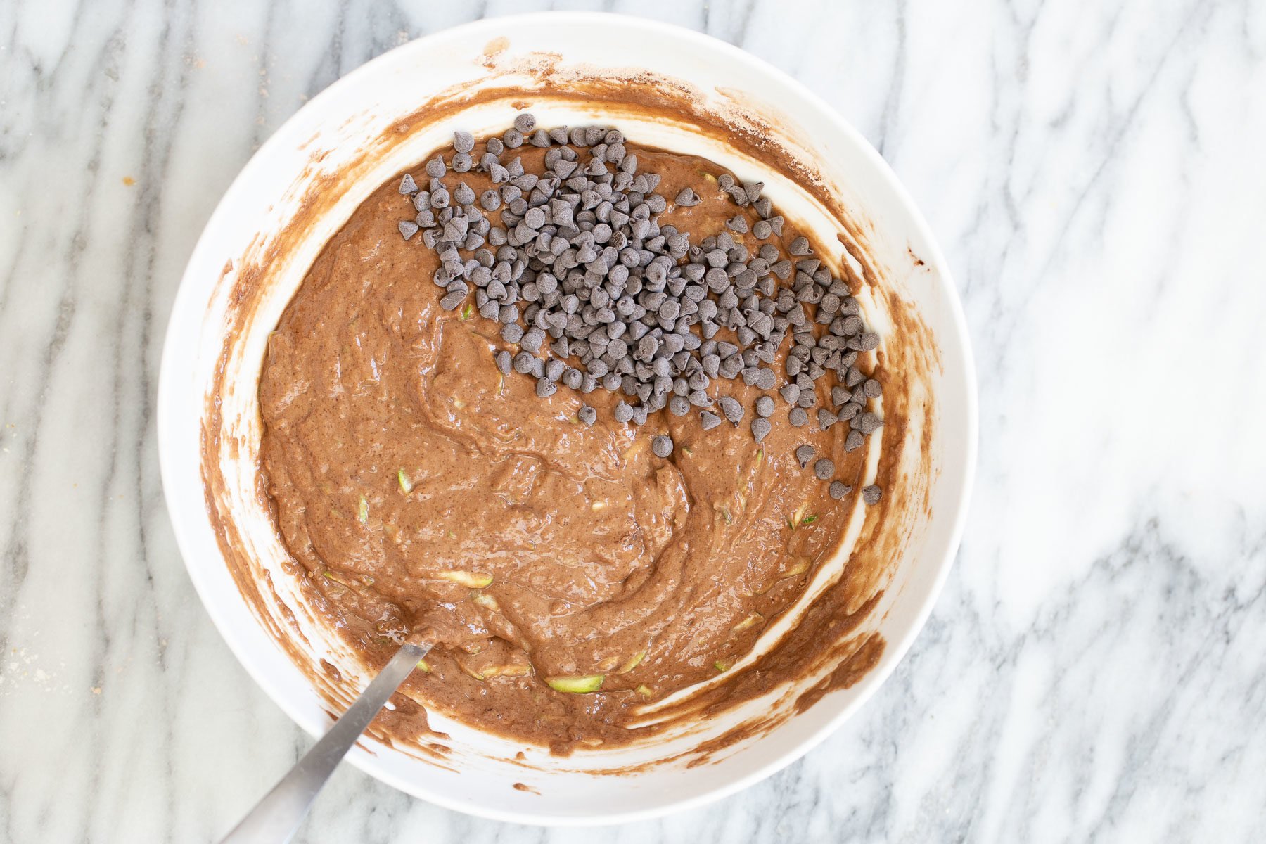 chocolate zucchini bread overhead shot of a white bowl with vegan zucchini bread batter sprinkled with chocolate chips