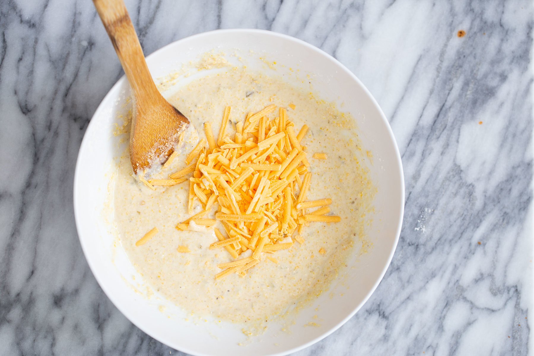 chili cornbread casserole cheddar shreds being stirred into cornbread batter