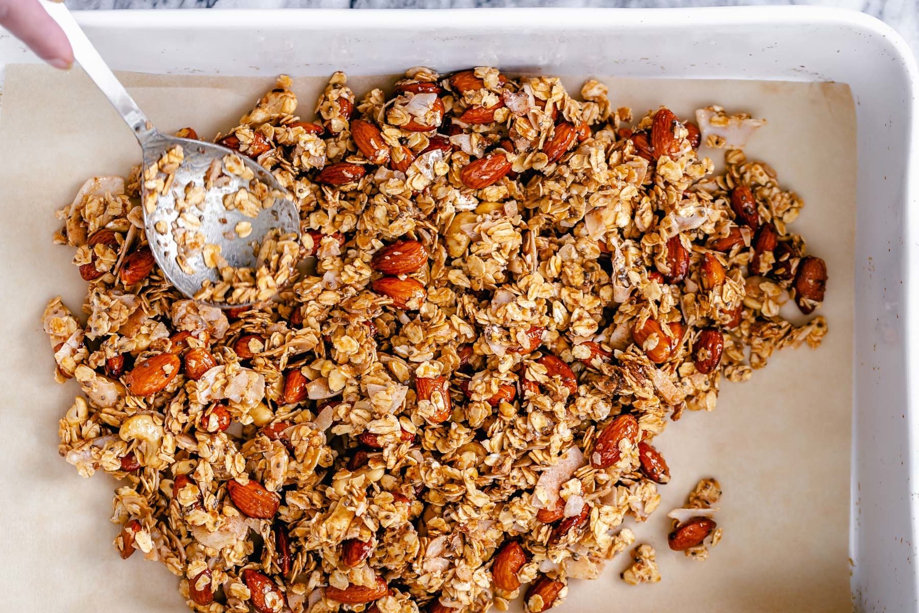 coconut granola almond coconut granola being spread onto a baking tray to make baked vegan coconut granola