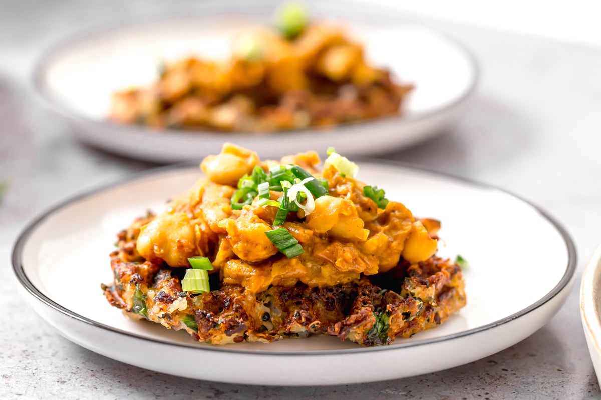side view of a vegan potato quinoa waffle being topped with smashed chickpeas