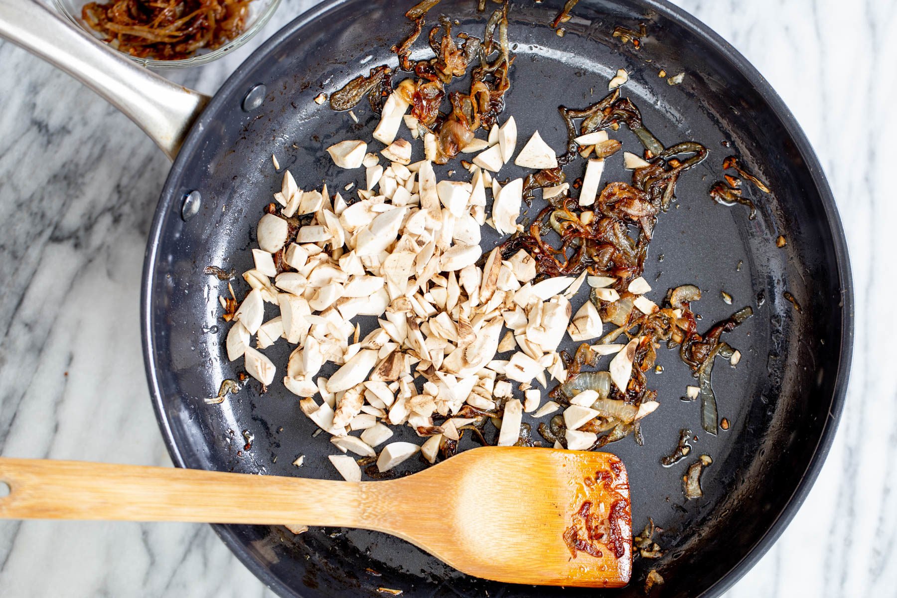 vegan skillet lasagan mushrooms being added to caramelized onions in a skillet