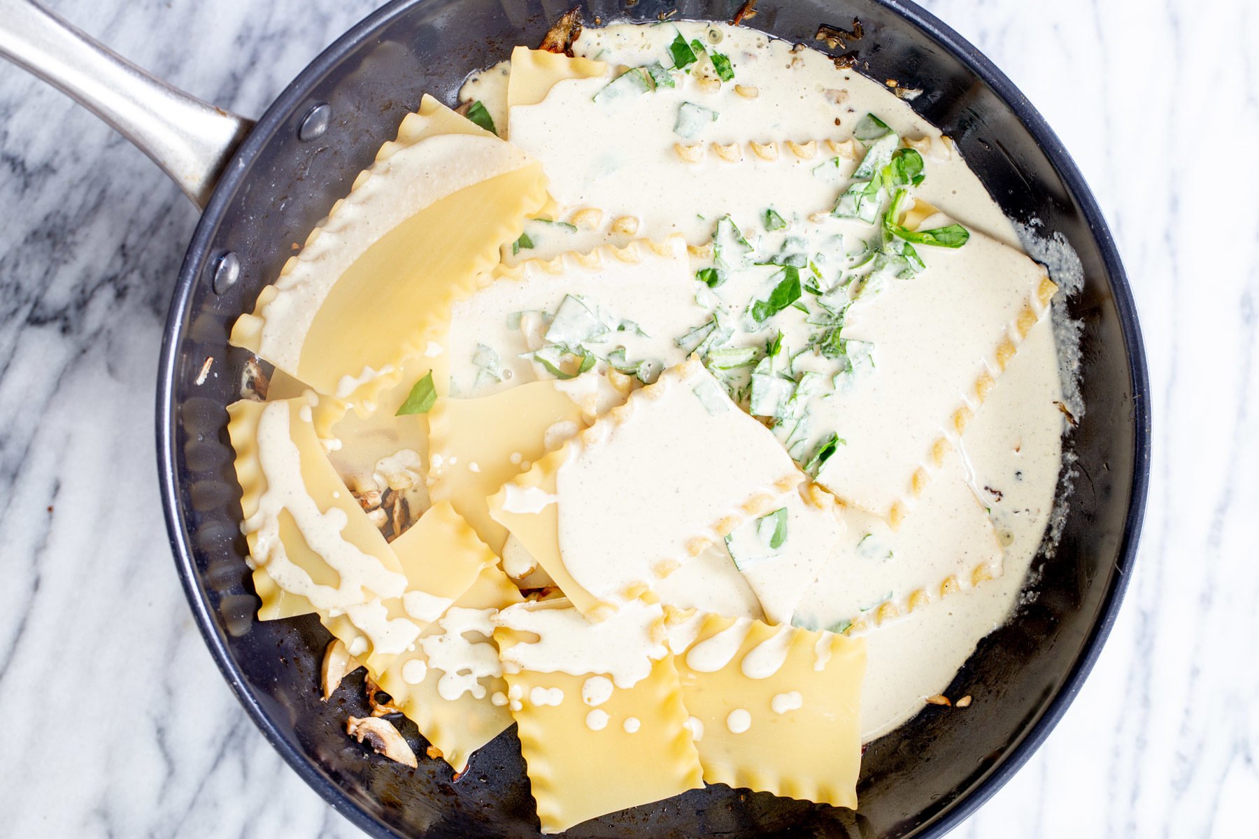 vegan skillet lasagna  vegan bechamel sauce being added to lasagna noodles and caramelized onion is a pan