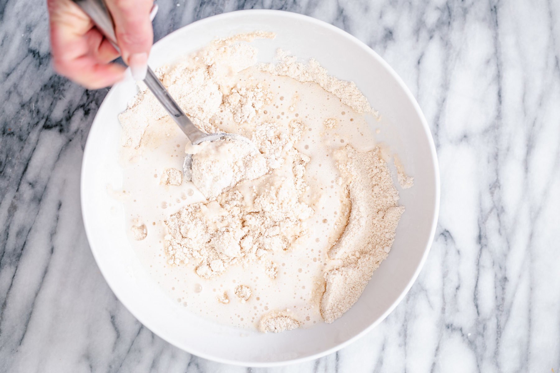 glutenfree donuts recipe  wet ingredients being stirred into dry donut ingredients in a white bowl