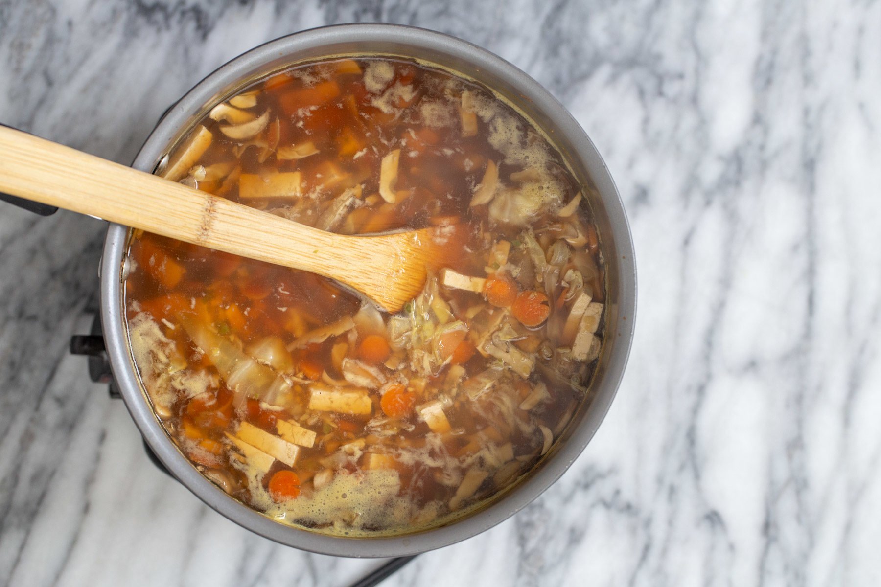 a wooden spoon stirring in a pot with vegan hot and sour soup