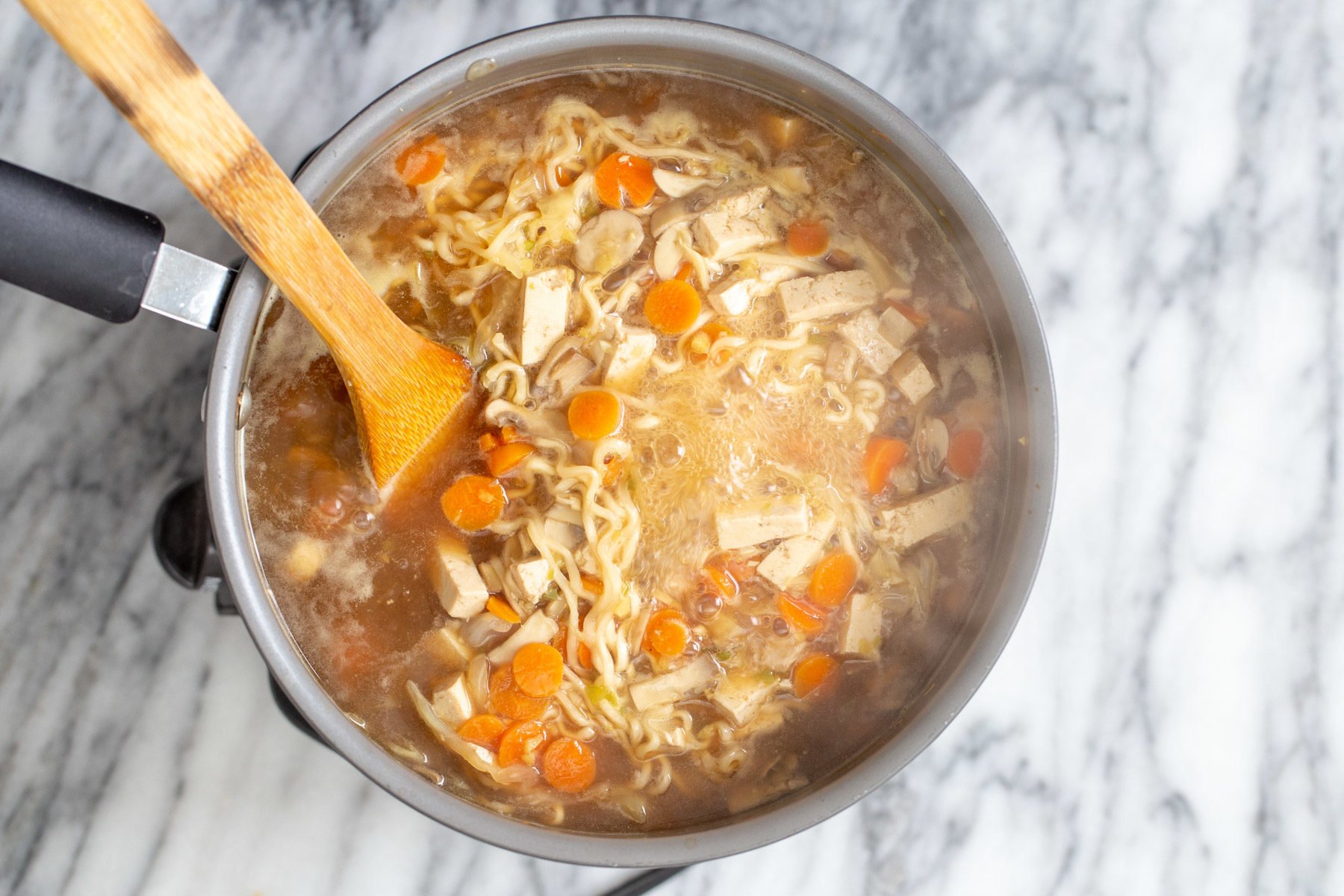 vegan hot and sour soup  a wooden spoon stirring in a pot with vegan hot and sour soup with ramen noodles