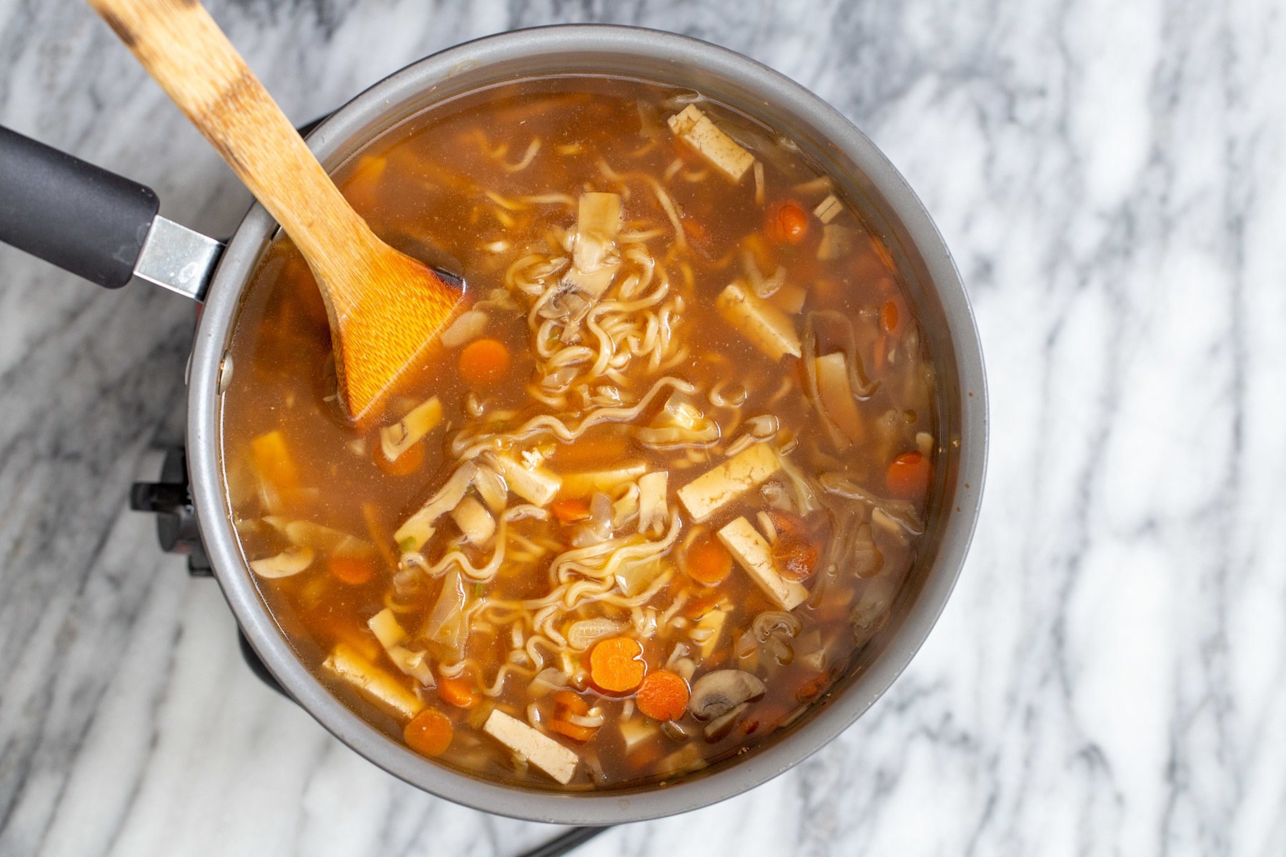 vegan hot and sour soup with ramen noodles in a silver soup pot with a wooden spoon