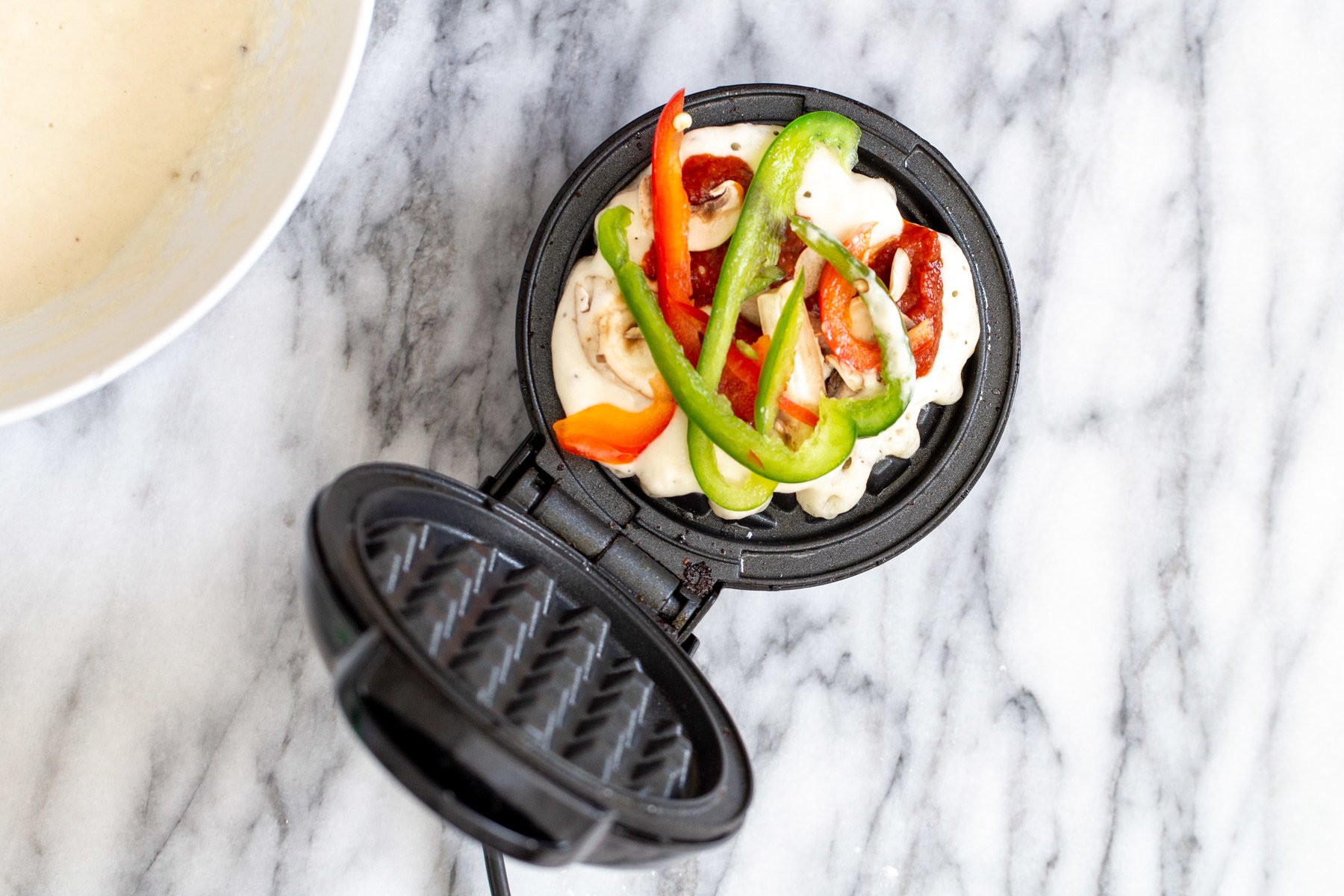 vegan pizza vegan pizza waffles batter in a waffle iron being topped with veggies