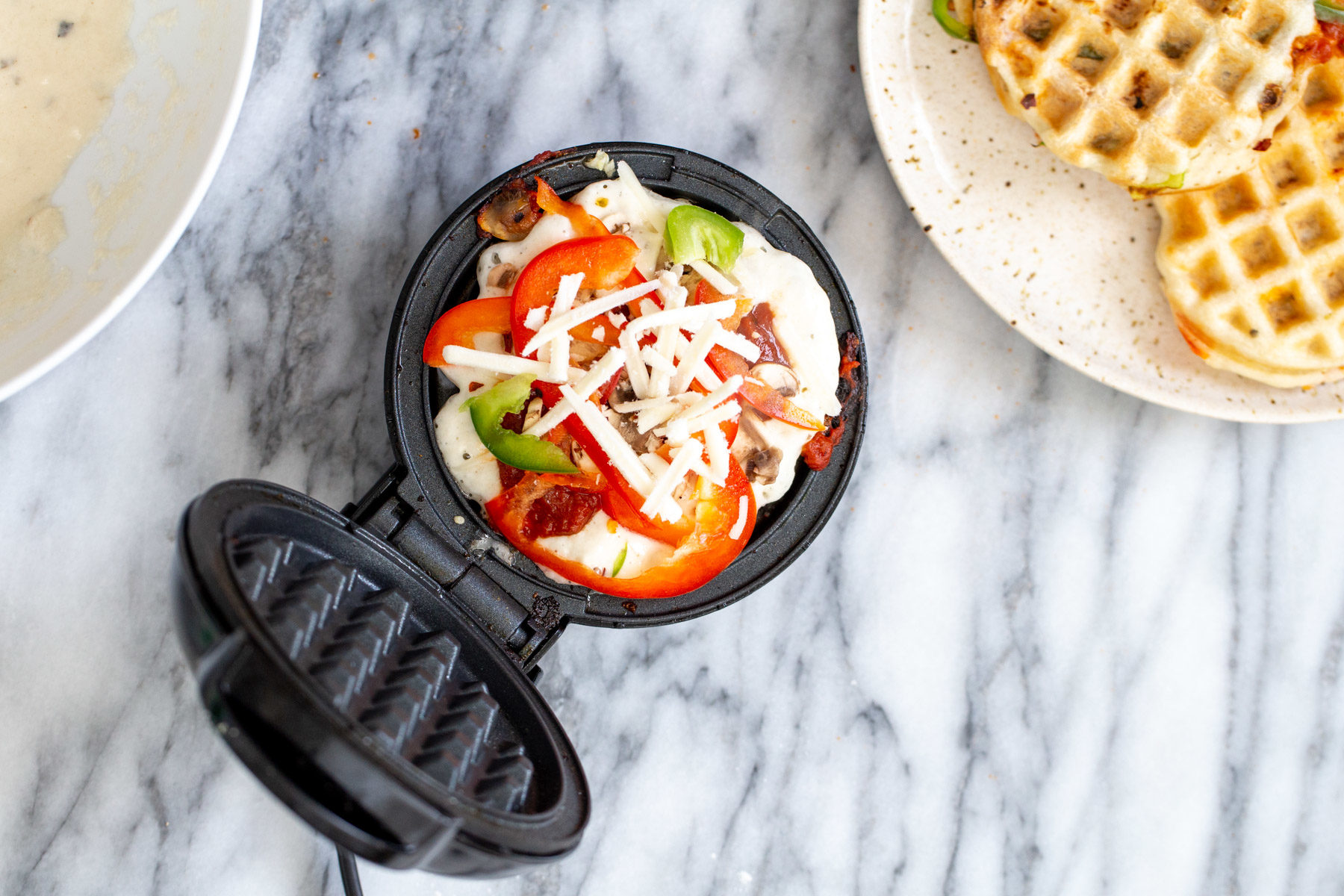 vegan pizza waffles vegan pizza waffle being topped with shredded mozzarella cheese