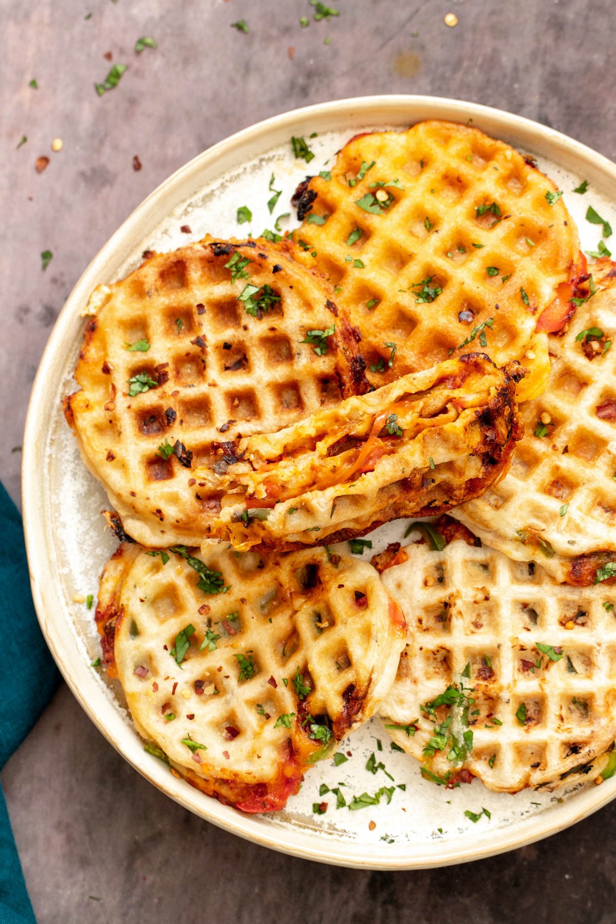 a plate with freshly baked vegan pizza waffles with one waffle being cut into half to reveal cheesy filling