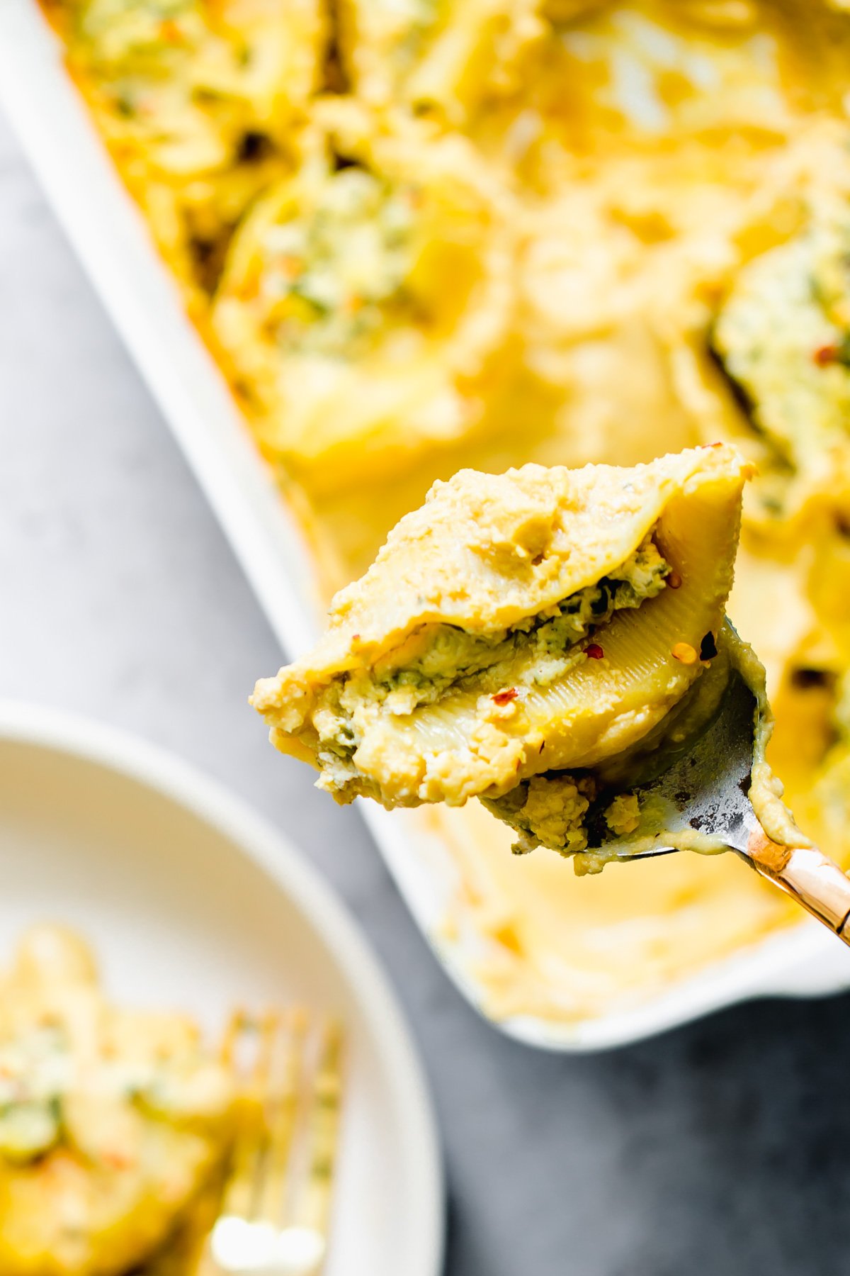 vegan stuffed shells a spoon holding a vegan stuffed shell filled with tofu ricotta