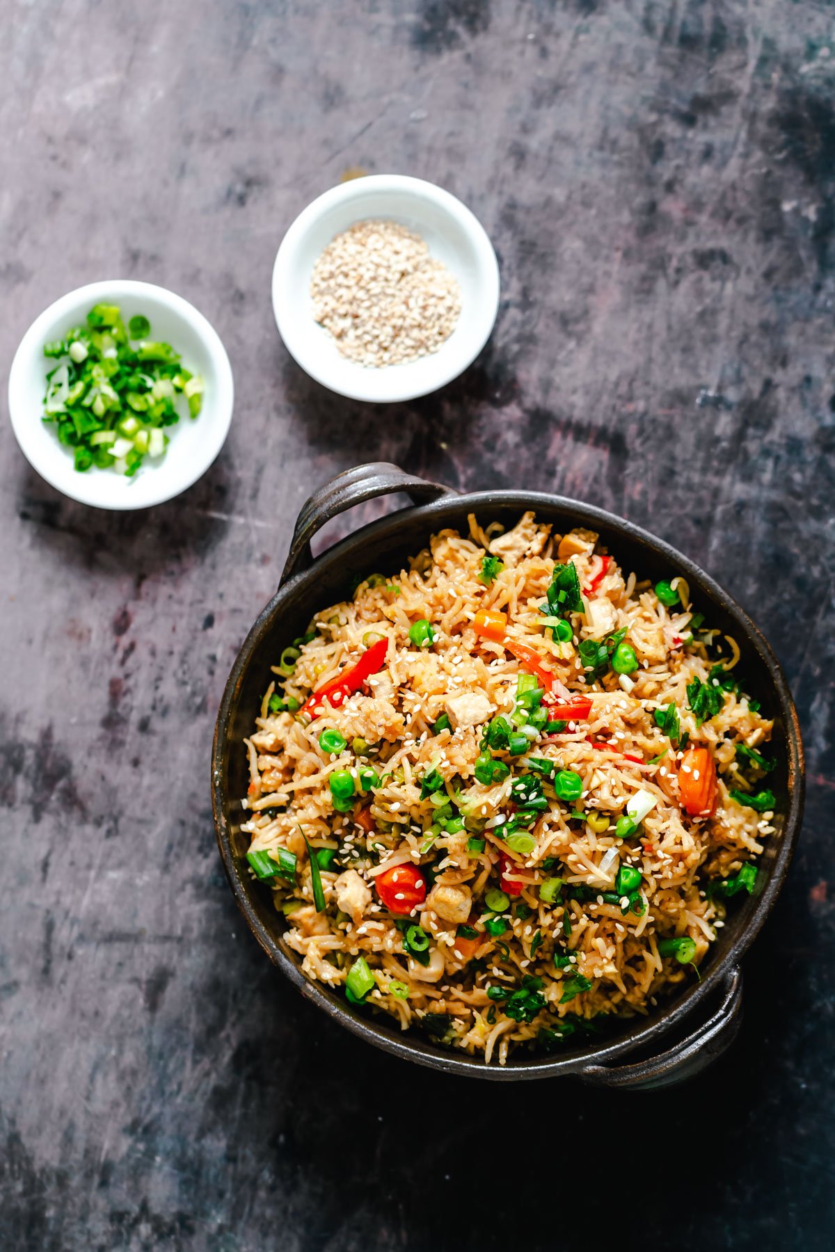Vegan Teriyaki Fried Rice served in a black dish with a side of sesame seeds and green onions