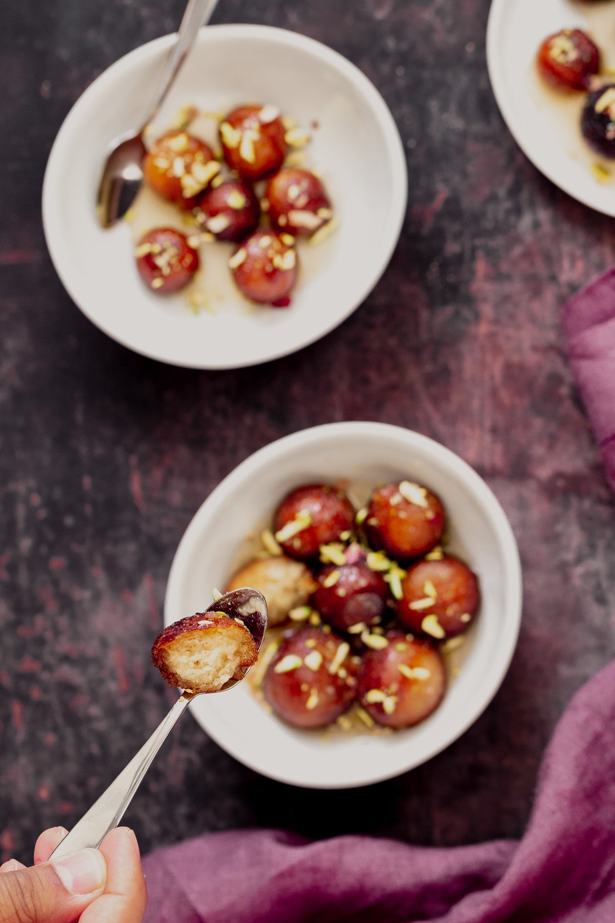 a small spoon with half a syrup soaked vegan Indian donut