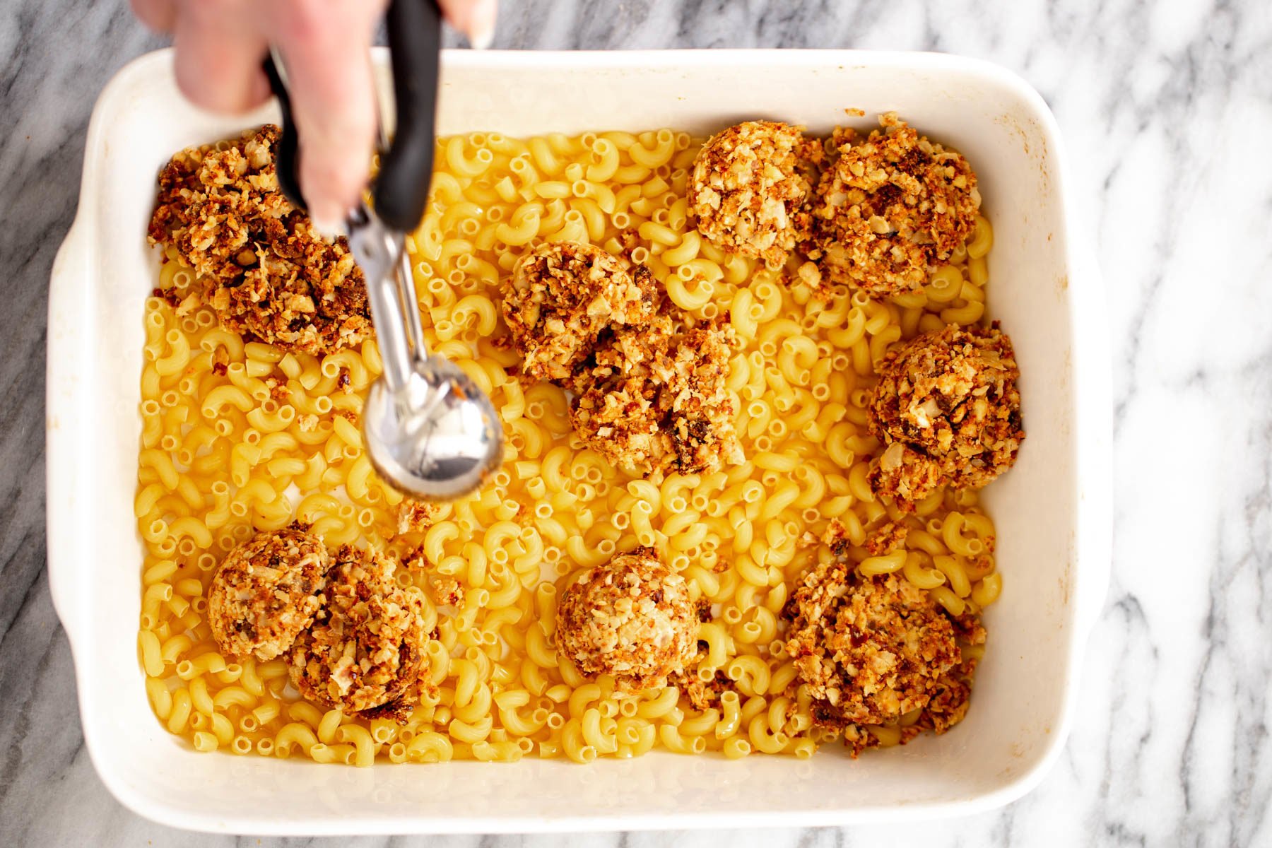 vegan taco meat being scooped on top of elbow pasta to make mac taco bake